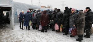 Refugees lined up at a tent in winter snow.